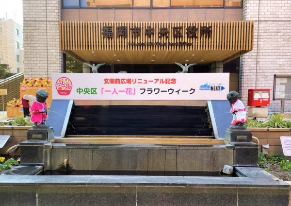 中央区役所玄関前広場に中央区「一人一花」フラワーウィークのタイトル看板を設置している様子