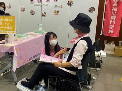 足のマッサージを体験している参加者に学生が話しかけている写真