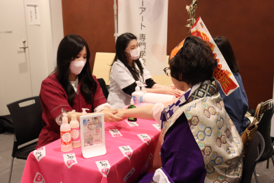 どんたくの衣装を着た参加者がハンドマッサージの体験をしている写真