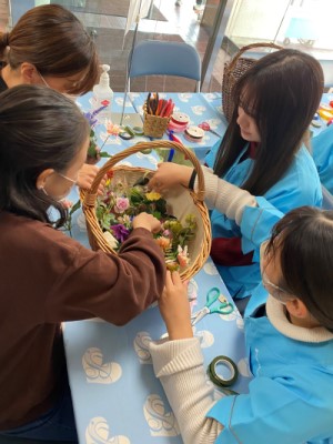 学生と一緒に造花を組み合わせて、ミニコサージュを作っているこどもの写真