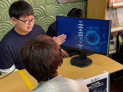 モニター上の入力画面を見せながら、占いの説明をする学生の写真