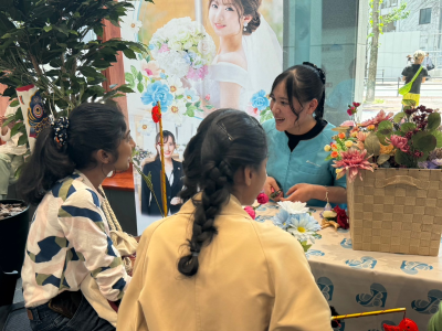 専門学校生が留学生にミニコサージュの作り方を丁寧に教えている写真