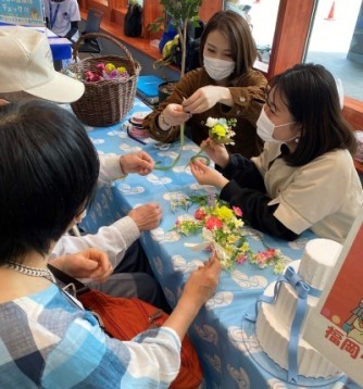 参加者が選んだ造花を、学生がコサージュの形に整えて見せている写真