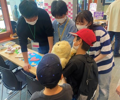 男の子がぬいぐるみを抱えながら学生の説明を受けている写真