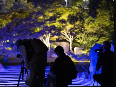 学生が明るさを調整しながら、青く照らされた庭を撮影している写真