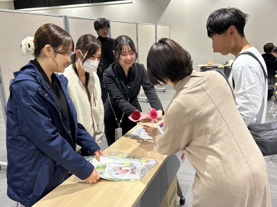 婚姻届けを提出したカップルに、祝福の言葉をかけながら一輪花を渡している学生の画像