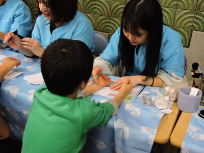 学生が小学生の手首にキラキラパウダーを使ってペイントしている画像