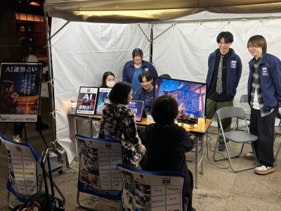 櫛田神社会場で、AIエンジニア専攻の学生が作成した「AI占い」を来場者に体験してもらっている画像