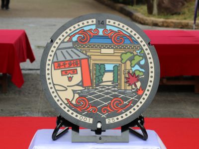 博多千年門に宿る妖精・せんねもんが門の中に招いているデザインのマンホールの写真