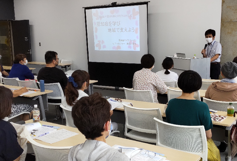 認知症サポーター養成講座の受講風景の写真。講師がパワーポイントを用いて説明し、参加者が真剣に聞いている様子の写真。