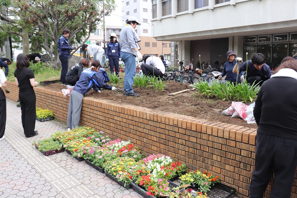 庁舎入口近くの花壇の植替え作業をする職員の写真