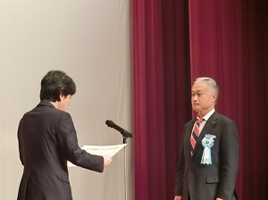 表彰式の様子の写真。表彰状を表彰者に渡すところ。