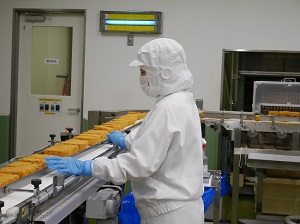 麺がベルトコンベアを流れている様子を従業員が見ている写真