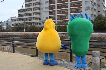 城南区シンボルキャラクターニッコりんとワルもんが樋井川を眺めている様子