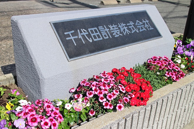 社名の入ったモニュメントの周りが花壇になっています