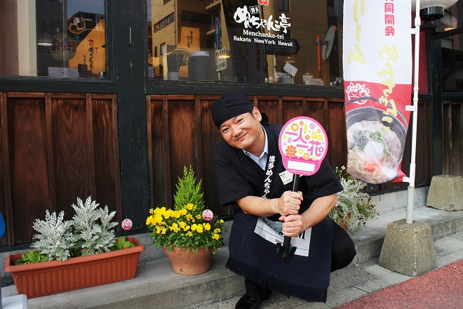 大将が一人一花ロゴのうちわを持って店舗前で写った写真