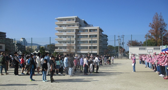 青空の校庭に集合した、赤と白のボーダーシャツ姿のWさんと子どもたち