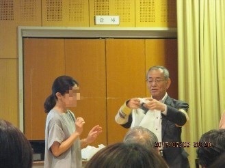 女性の前で三角巾を作ってみせる講師の様子