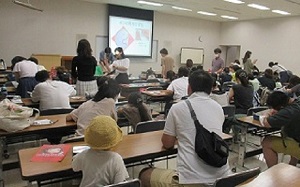 ７×４列に並んだ長机に二人ずつ着座する参加者でいっぱいになった講座室内部。