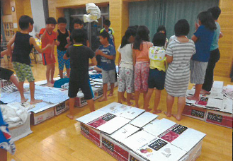 公民館に作った段ボールベッドと、じゃんけんをする子どもたちの写真
