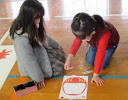 目隠しをして協力して福笑いを楽しむ女の子2人