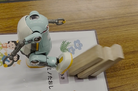 指示通りに、歩いて積み木をキックして倒しているロボットの写真