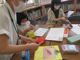 教えてもらって折り紙をつくる子どもの画像