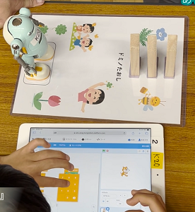小学生が手のひらサイズのロボットを前に、タブレットで指示をプログラミングしている写真
