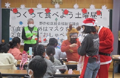 サンタとトナカイと中学生が子どもにプレゼントを渡す画像