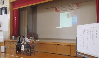 保護者がステージのスクリーンにプロジェクターで資料を投影するための準備をしている様子