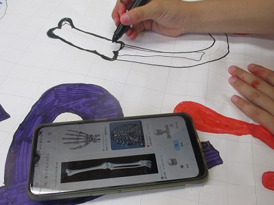 子どもがスマホの骨格画像をみながら絵を描く画像