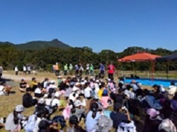 前に立つスタッフを紹介、子どもたち全員は芝生に座っている様子