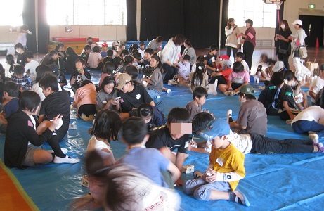 ブルーシートの上で牛乳パック灯篭を制作中の子どもたちの写真