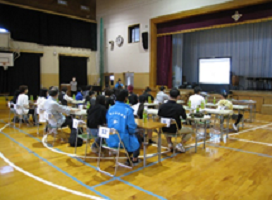 体育館に長机を並べて、中学生と地域の方がペアで座っているようす。