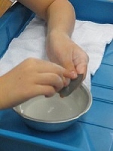 容器の水で、勾玉の艶出し磨きをする子どもの手元写真