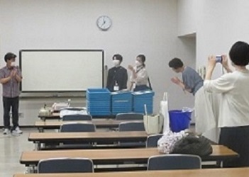 左の塾長から真ん中の専門員お二人を紹介、右はお礼のお辞儀をする主事と撮影するスタッフ