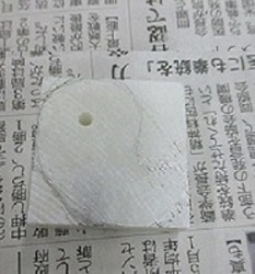 一角に小さな穴があけてある勾玉材料の四角く白い石に、鉛筆でカタチを書き込んだ写真