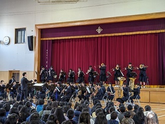 ステージで中学校吹奏楽部が演奏するのを座って聴いている小学生