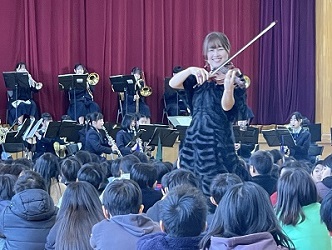聴き入る子ども達の中に歩み入って笑顔で演奏するプロのバイオリニスト