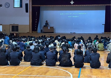 壇上左手に立ち、中央のプロジェクターに会社の様子を映しながら公演している講師