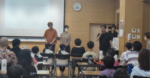 長机いっぱいの家族連れの前に立つ団体や公民館のスタッフと、紹介を受ける二人の講師の写真