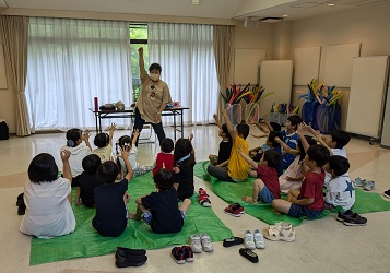 前に立つ講師と、シートに座ってジャンケンをして遊ぶこども達