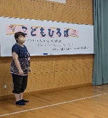 こどもひろばと書いたホワイトボードを背に、子ども達にお話をする公民案主事