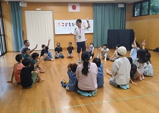 大人も子どもも講師を真ん中に一つの輪になって座り、フルーツバスケットを楽しむ様子。