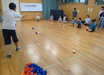 簡易コートの外で聴く子ども達に、ボッチャのルールを説明する講師