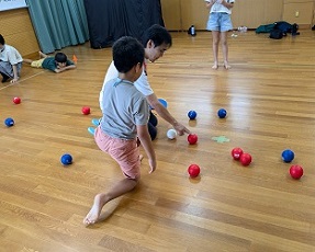 メジャーで球の距離を計測中の講師の手元を、待ちきれずに見に来る子ども。