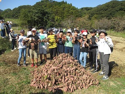 収穫したたくさんのお芋の後ろでポーズを取る子どもたちの様子