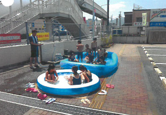 駐車場に広げたビニールプールで遊ぶ子どもたちの写真