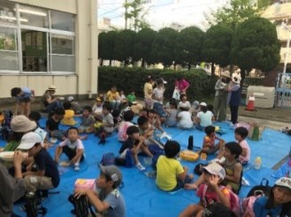 屋外のブルーシートでカレーを食べる参加者たちの写真