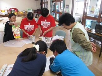 テーブルを囲んでレシピを読む子どもたちの写真